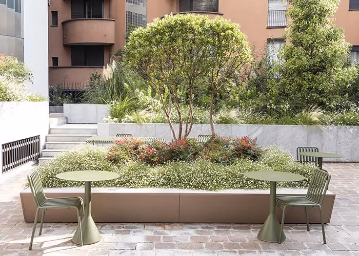 Large modular bed with a central ornamental tree, small white flowers and green side tables in a modern urban courtyard.