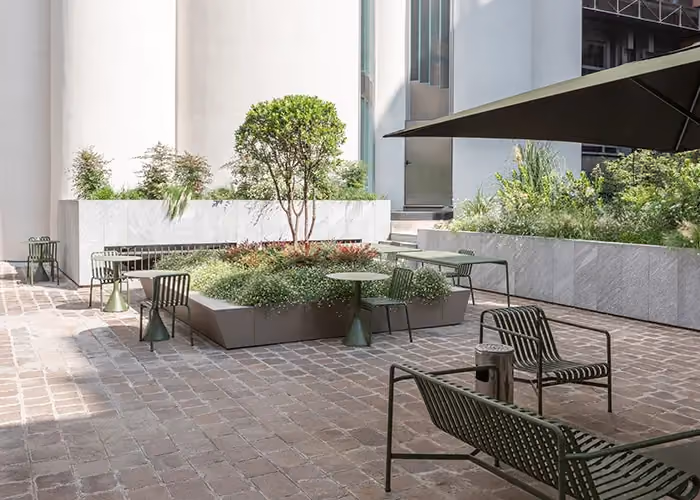 Elegant outdoor space with stone paving, modern seating and modular beds holding trees and decorative plants.