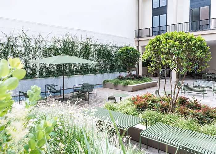 Contemporary courtyard with green outdoor seating, a parasol and large modular beds with trees and ornamental planting.