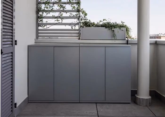 Grey four-door storage unit installed on a terrace balcony beneath a planter.