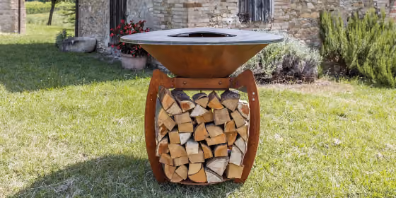 Braciere circolare in acciaio corten su base svasata con legna accatastata sotto
