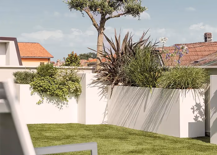 White corner planters set along a garden with a manicured lawn, holding shrubs and ornamental plants.