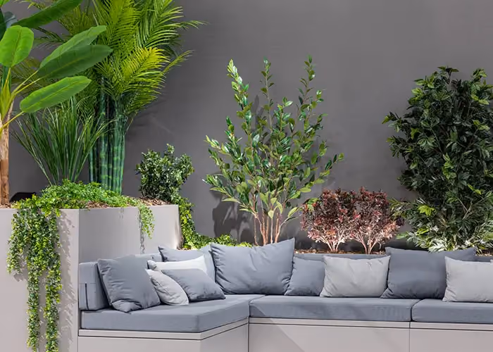 Modular outdoor sofa with grey cushions and large integrated planters holding green decorative plants, on a minimal dark ground.