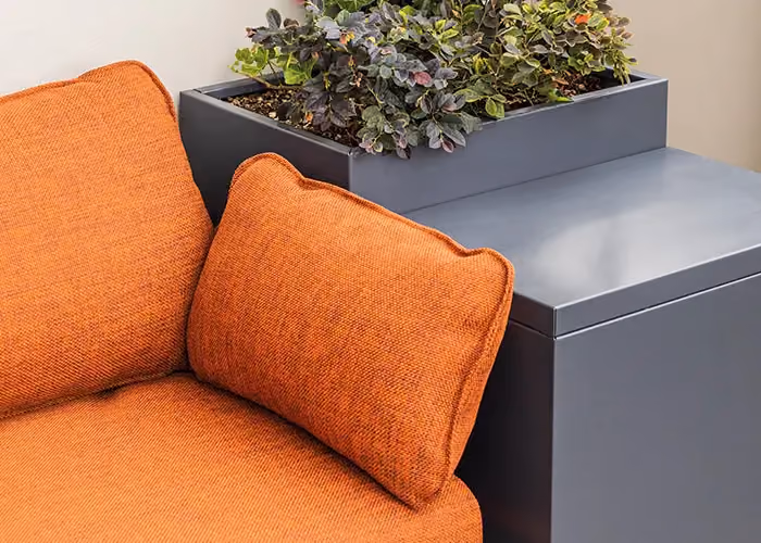 Detail of a modular outdoor sofa with orange cushions, a dark grey metal storage frame and an integrated planter.