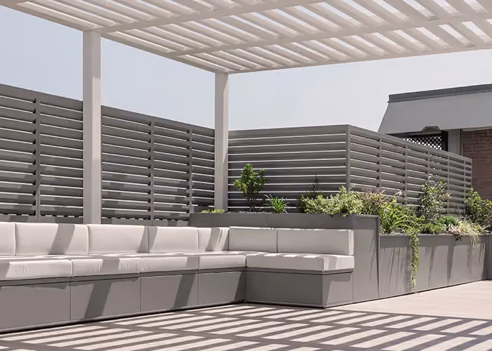 Modern terrace covered by a pergola, with a long modular outdoor seat with pale cushions and integrated planters.