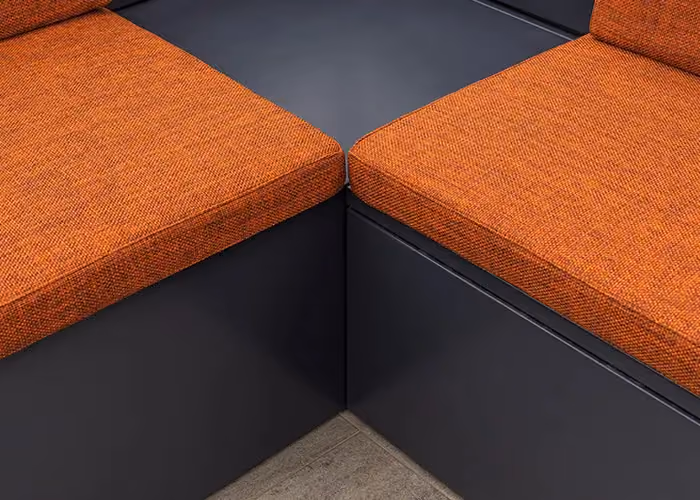 Close-up of modular outdoor seating with orange cushions and a geometric dark metal frame.
