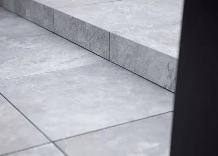 Detail of a step clad in grey stone-effect flooring, minimal in design.