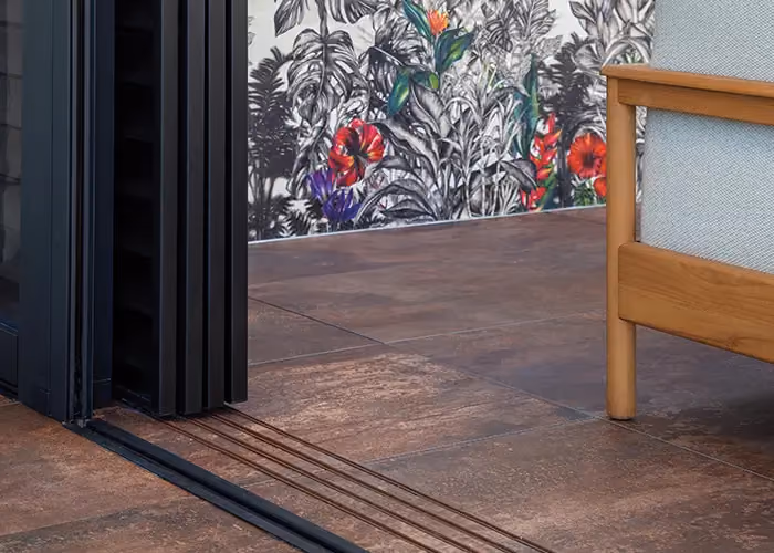Detail of dark stone-effect flooring with a recessed track for a sliding door, and a decorative floral wall behind.