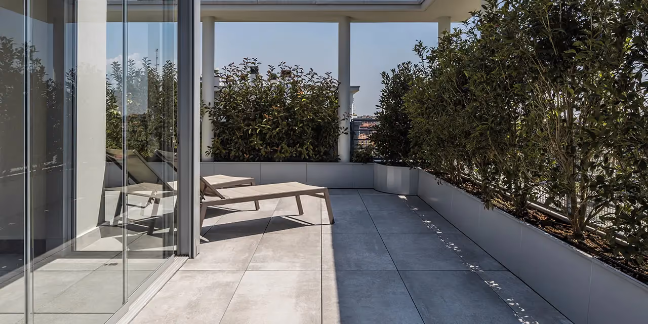 Raised grey decking on a long terrace, bounded by a continuous glazed wall