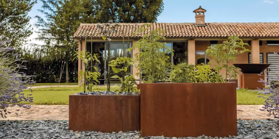 Fioriere alte in acciaio corten allineate davanti a un casale in pietra