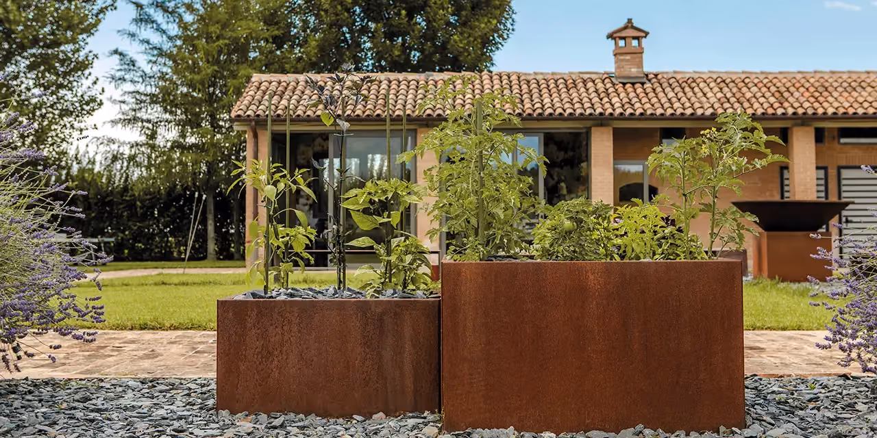 Fioriere alte in acciaio corten allineate davanti a un casale in pietra
