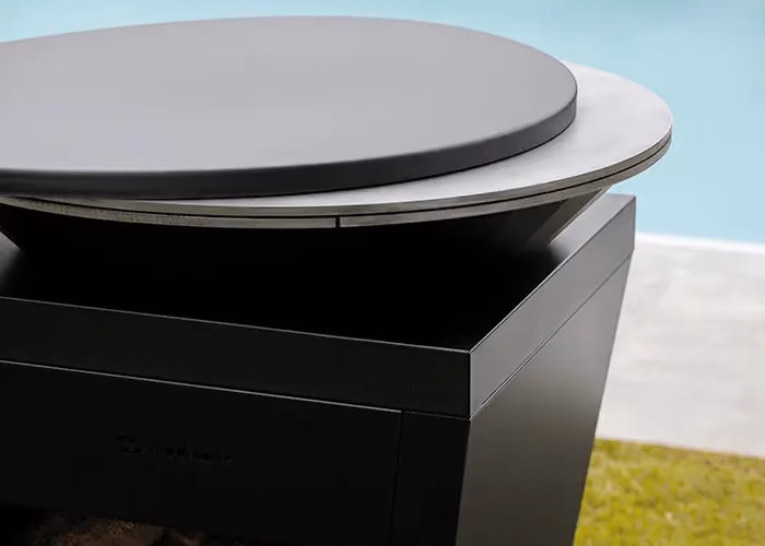 Detail of the circular top of a modern outdoor barbecue in black metal, with a raised cooking surface.
