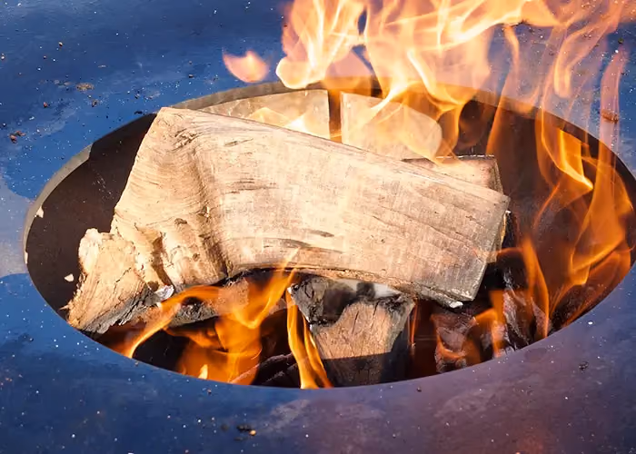 Close-up of logs burning inside a circular black metal fire pit.