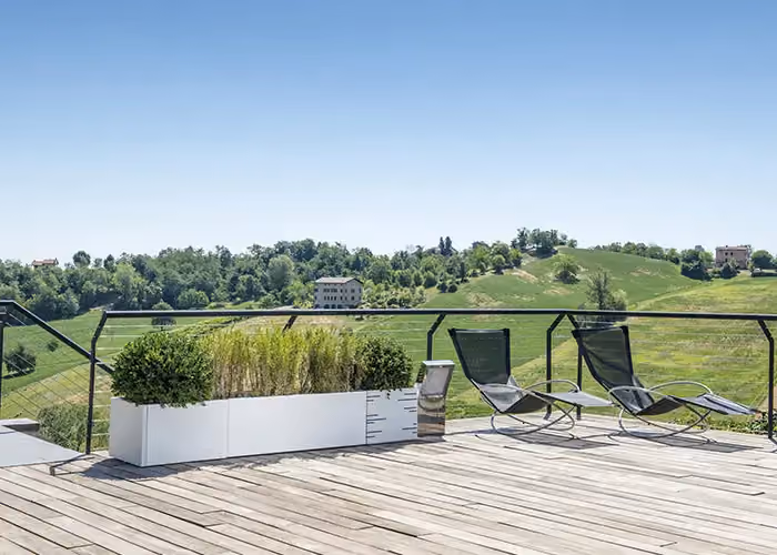Panoramic wooden terrace with sun loungers and a long white modular planter holding shrubs and ornamental planting.