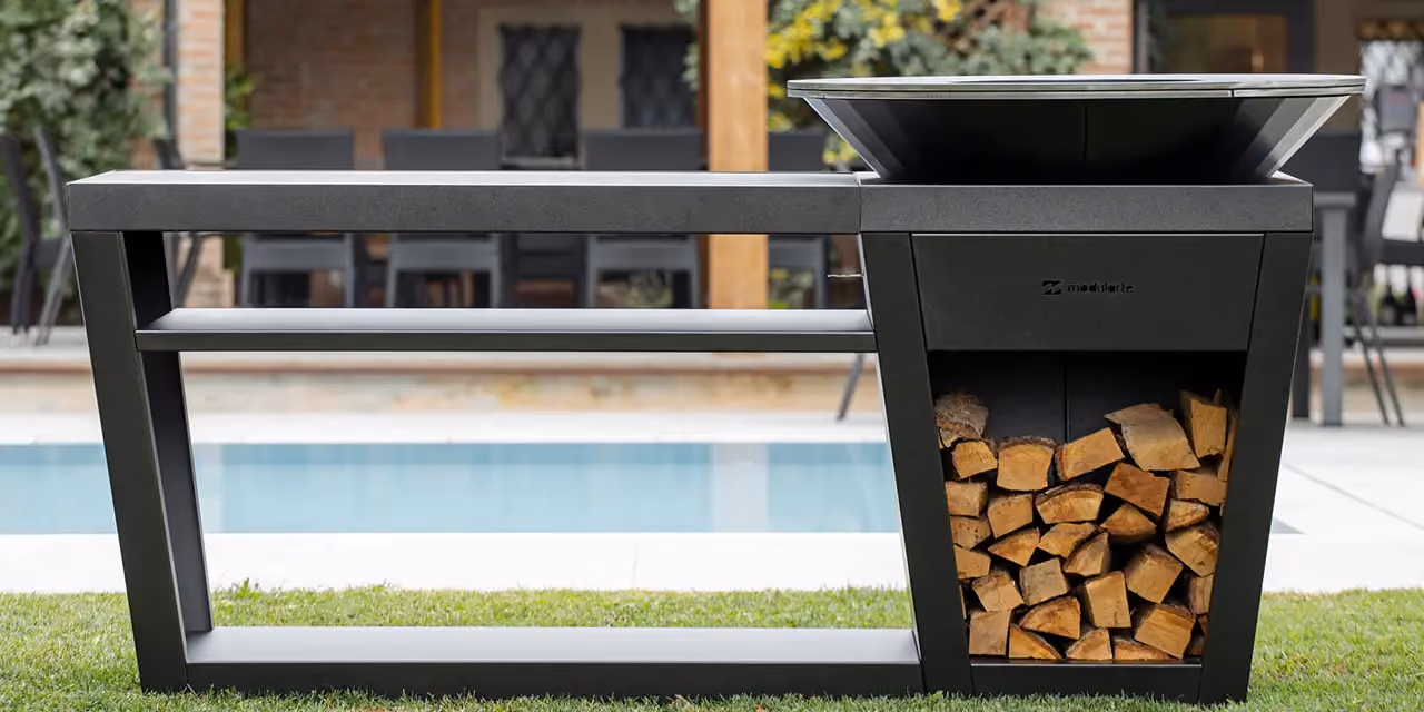 Outdoor island kitchen with a hob, a log bay, and a swimming pool behind