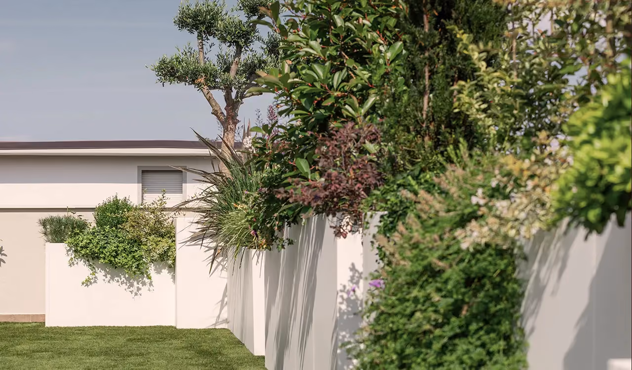 Side close-up of large white modular planters with green plants and lush shrubs, set along the edge of a lawned garden.