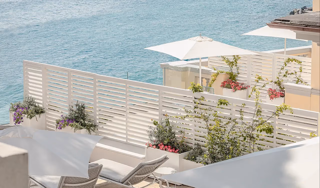 Seafront terrace with white slatted screens, sun loungers and flowering planters