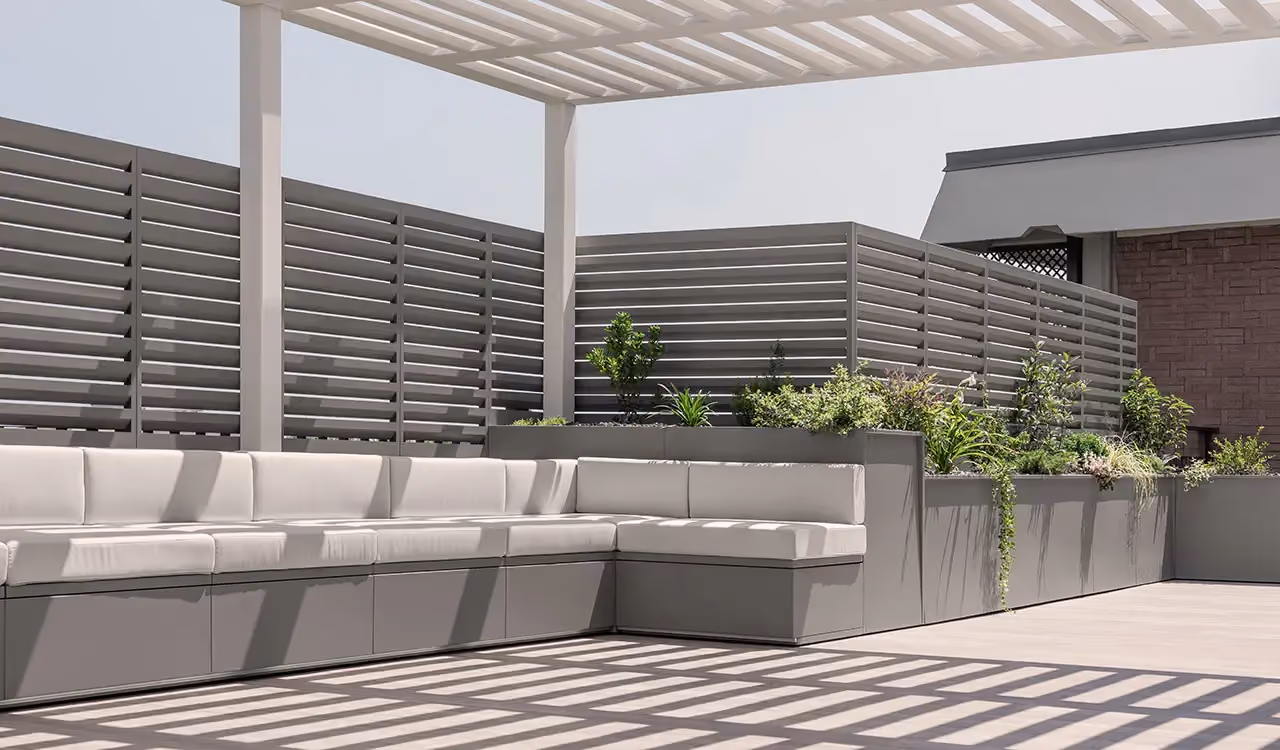 Terrace under a pergola with grey sofas and tall planters used as screening